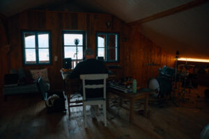 Foto von Künstler vor dem Laptop in Studio Setup in Zimmer mit Blick auf den See.