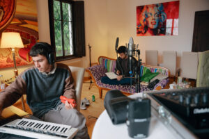 Foto von zwei Künstlern bei einer Songwriting Session in einem großen Zimmer mit Fenster zum Wald.